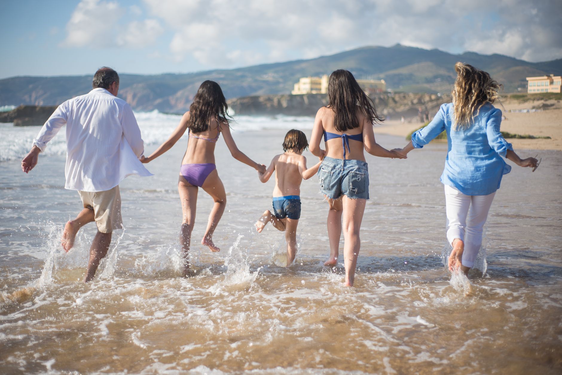 Famiglia che corre insieme sulla spiaggia al mare durante una giornata di sole