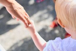 Bambino di spalle tiene la mano di un adulto con anello nuziale