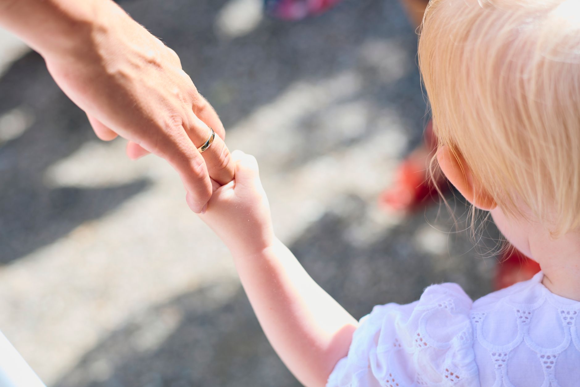 Bambino di spalle tiene la mano di un adulto con anello nuziale