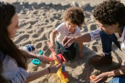 Famiglia con bambino che gioca con giochi di sabbia in spiaggia, simboleggia vacanza con bambini