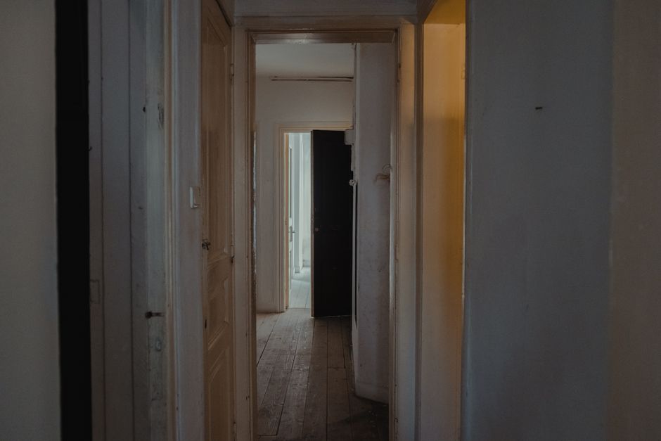 Corridoio lungo e sobrio di una casa vuota con porte chiuse e aperte, luce naturale fioca