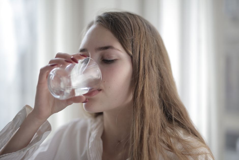 Giovane donna che beve acqua, simbolo di idratazione e benessere durante il ciclo in estate