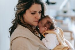 Mamma con espressione riflessiva abbraccia un neonato, mostrando un momento di fragilità e cura