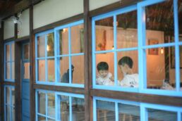 Due bambini mangiano insieme al tavolo all'interno di un locale con grandi finestre blu