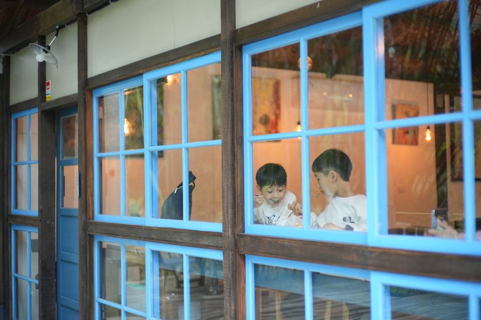 Due bambini mangiano insieme al tavolo all'interno di un locale con grandi finestre blu