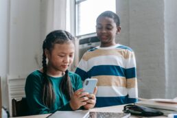 Due bambini che usano insieme uno smartphone, in un ambiente domestico luminoso