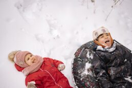 Due bambini sorridenti in abbigliamento invernale giocano sulla neve con slittino