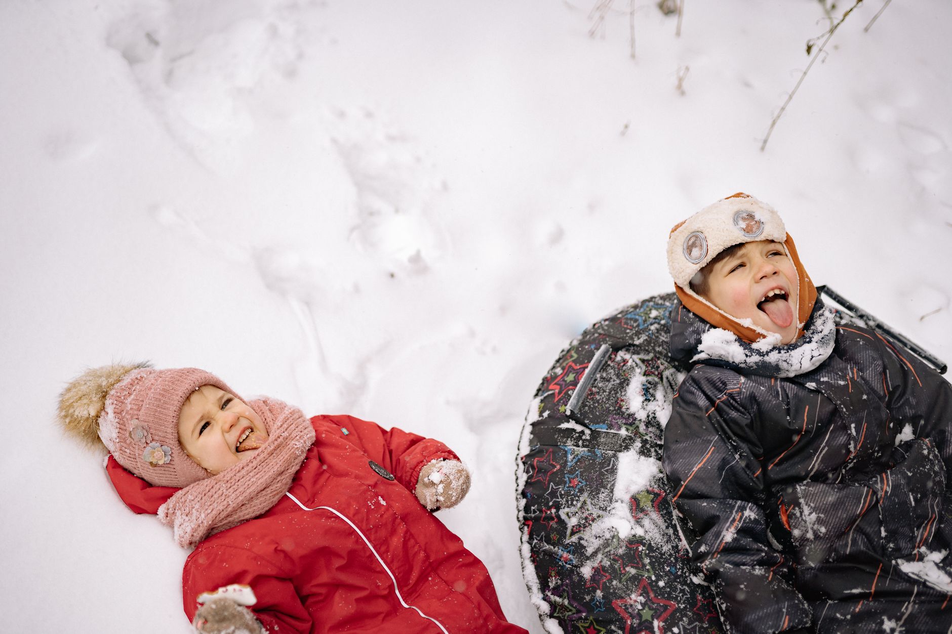 Due bambini sorridenti in abbigliamento invernale giocano sulla neve con slittino