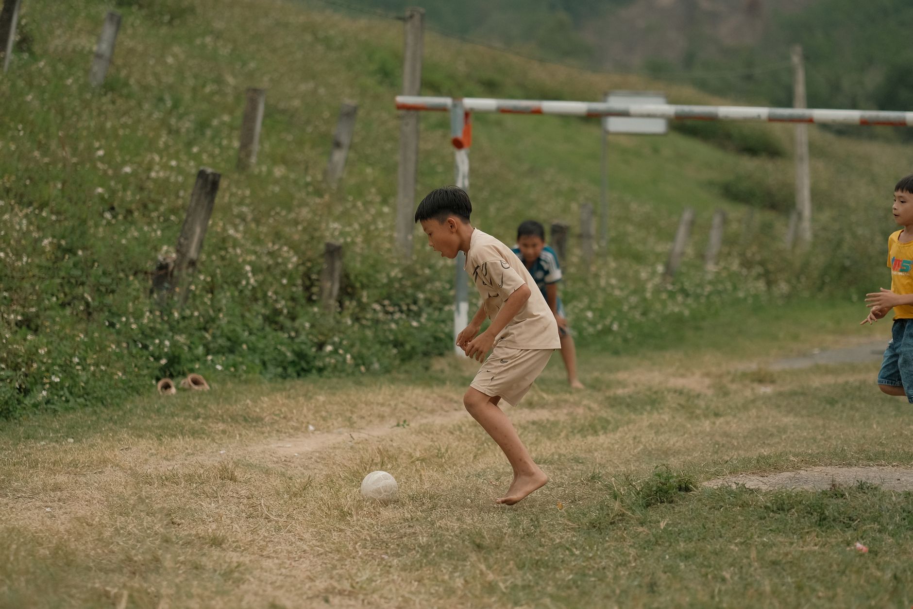 Bambini che giocano a calcio all'aperto su un campo di terra, in un ambiente naturale.