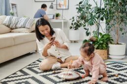 Mamma che usa lo smartphone mentre il bambino gioca sul tappeto in soggiorno