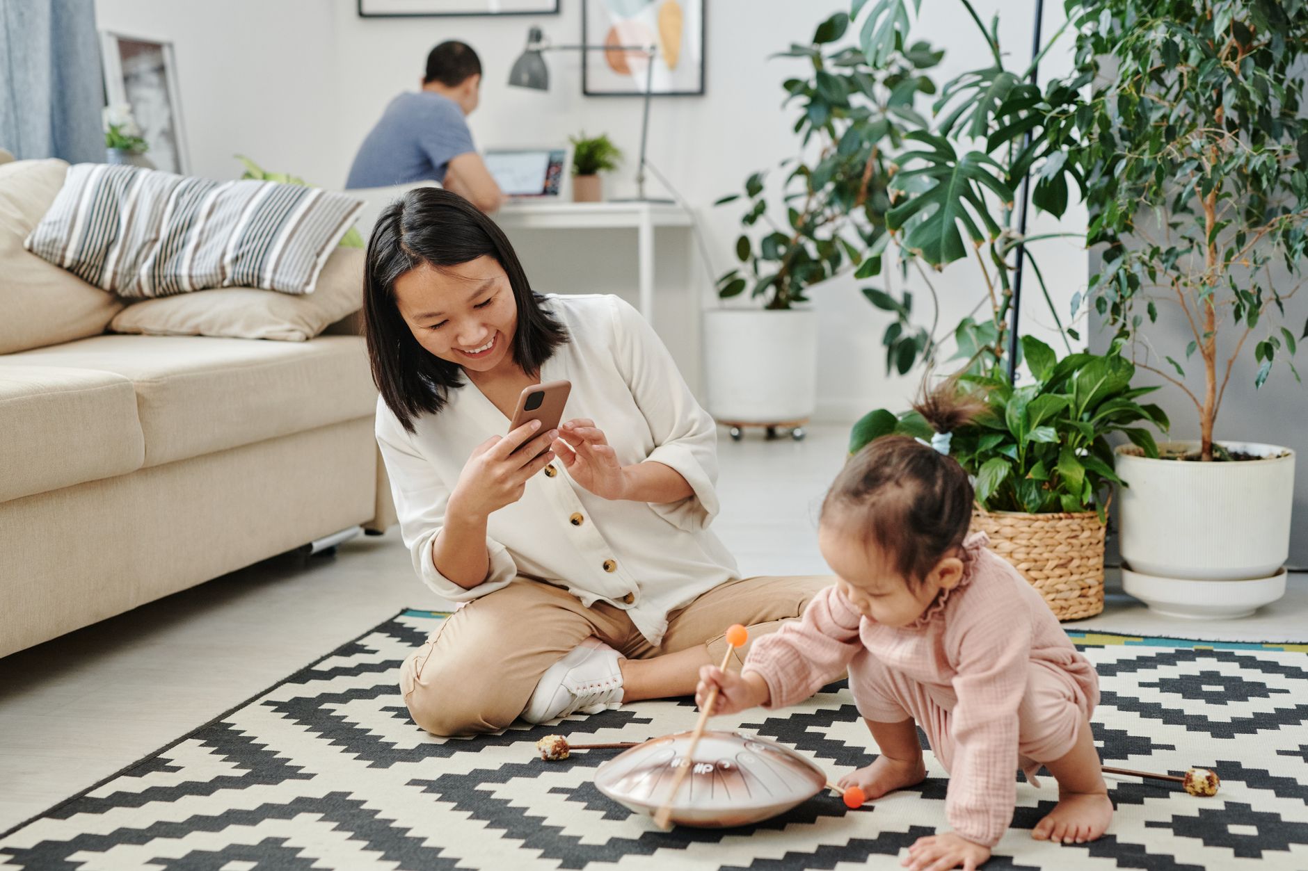 Mamma che usa lo smartphone mentre il bambino gioca sul tappeto in soggiorno