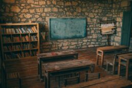 A rustic classroom with wooden benches, a chalkboard, and a bookshelf, symbolic of education and learning.
