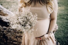 Dettaglio di una donna incinta in abito aderente beige che tiene un mazzo di fiori delicati