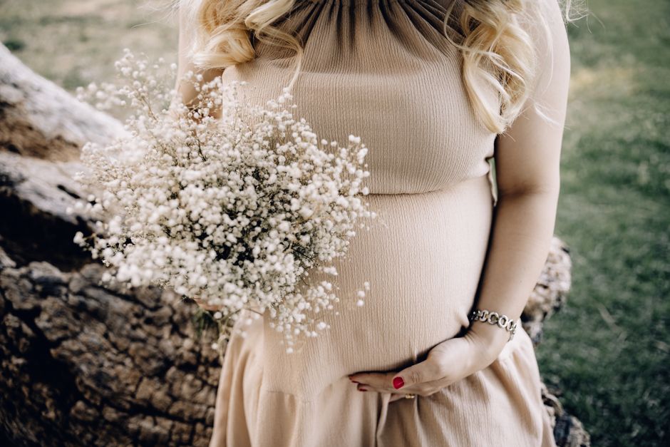 Dettaglio di una donna incinta in abito aderente beige che tiene un mazzo di fiori delicati