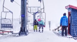 Due bambini con equipaggiamento da sci accanto a una seggiovia in una stazione sciistica innevata