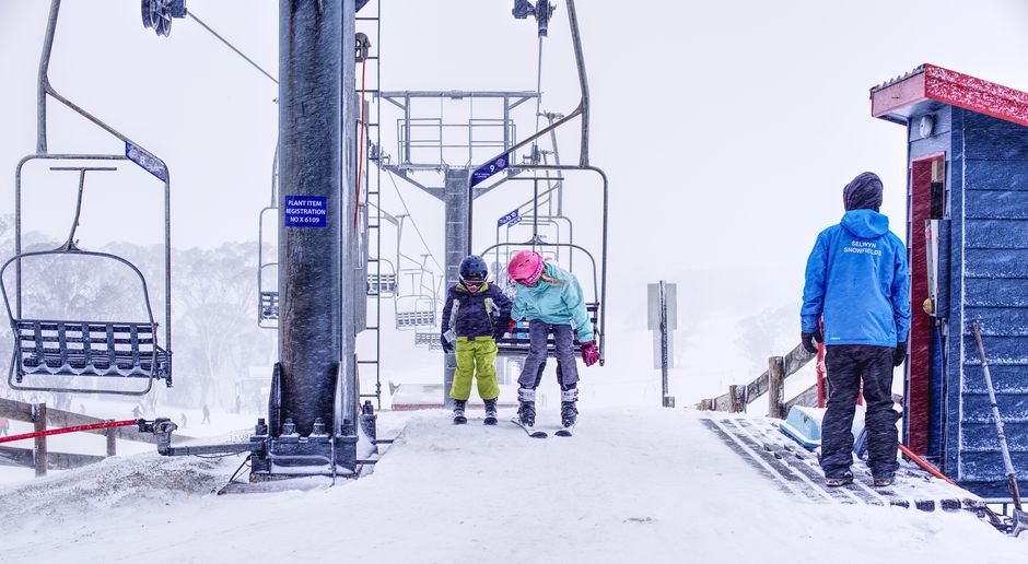 Due bambini con equipaggiamento da sci accanto a una seggiovia in una stazione sciistica innevata