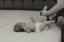 Neonato disteso in pannolino mentre una mano adulta gli allaccia le scarpe