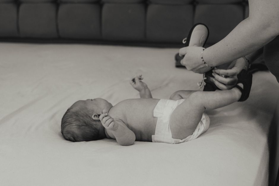 Neonato disteso in pannolino mentre una mano adulta gli allaccia le scarpe