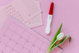 Calendario ciclico con test di ovulazione e fiori bianchi su sfondo rosa