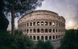 Veduta orizzontale del Colosseo a Roma con vegetazione e cielo al tramonto