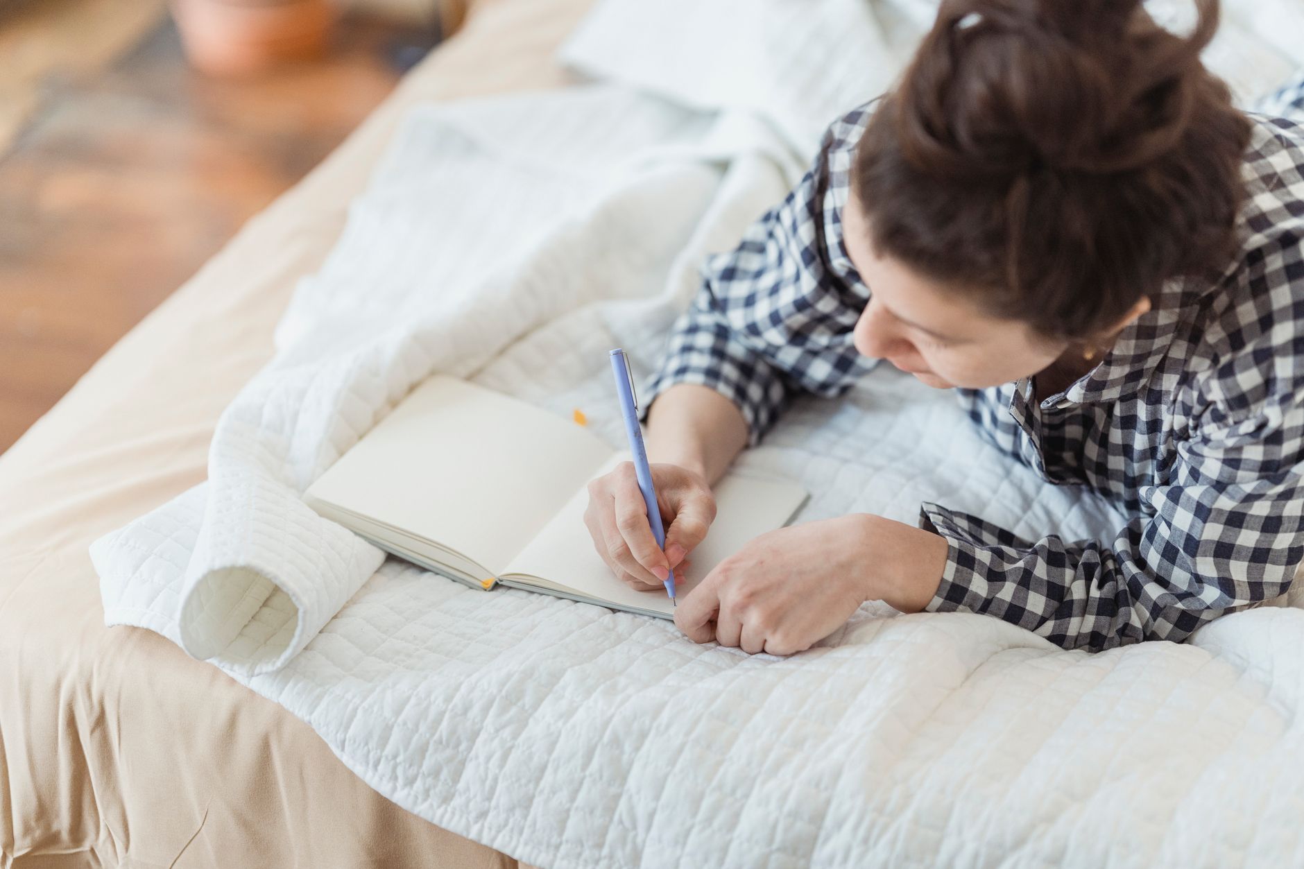 Persona che scrive in un diario stesa su un letto con coperta chiara